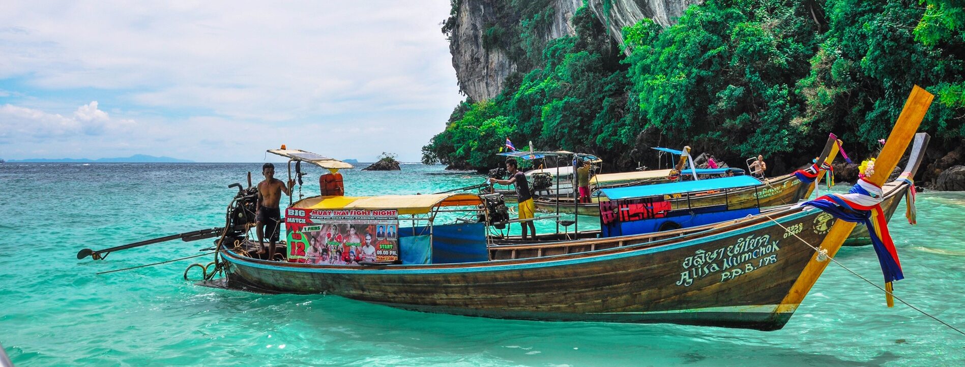 Barco tradicional longtail amarrado en aguas turquesas cerca de acantilados de piedra caliza en Phang Nga, Tailandia.